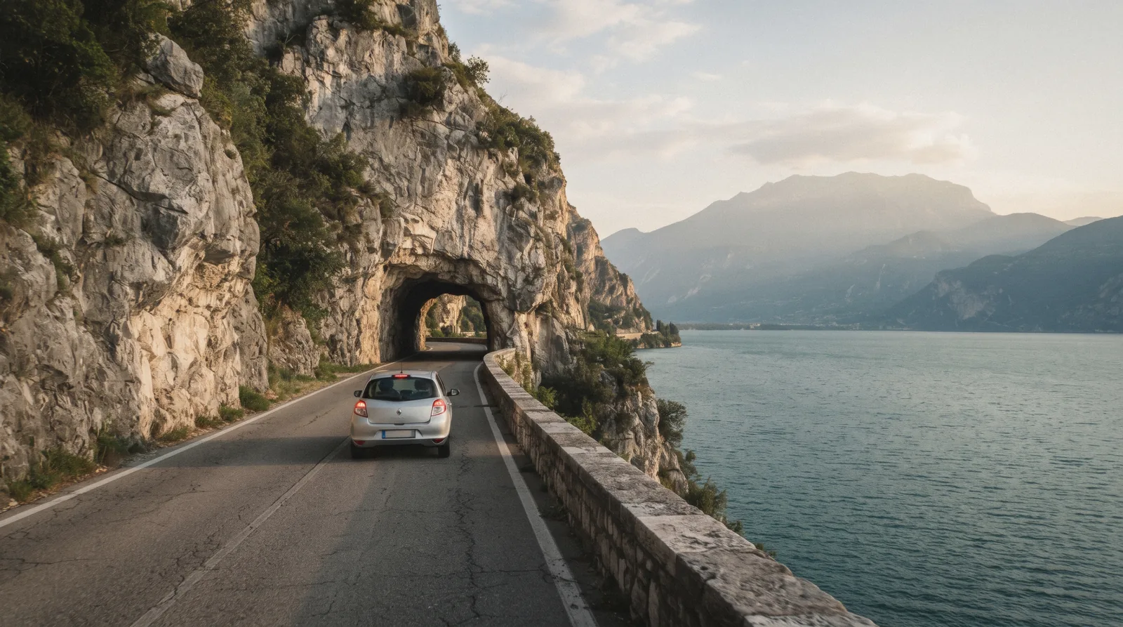 A small car on the Gardesana lakeside road below limestone cliffs on Lake Garda, Italy