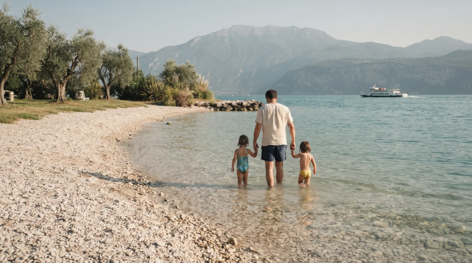 A parent and two children wading at a pebble beach near Bardolino on Lake Garda, Italy