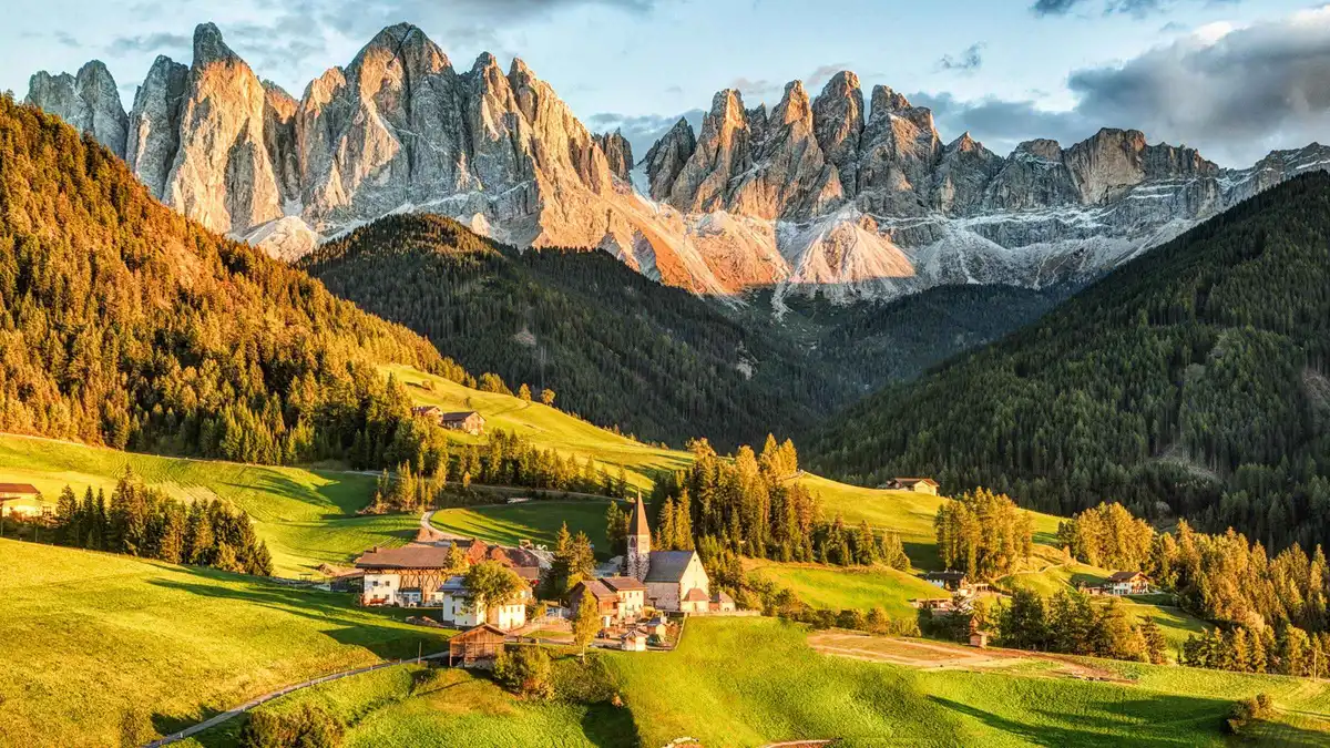 Jagged Dolomite peaks above green meadows and a small church in a valley at golden hour