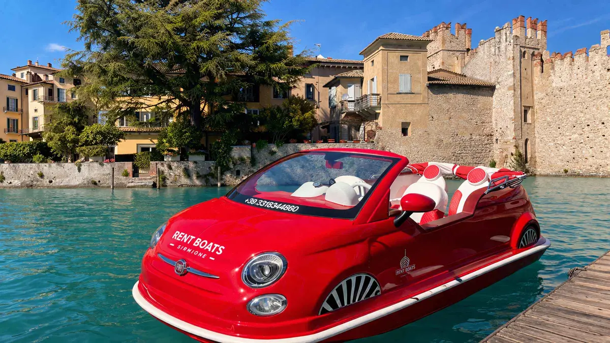 A red Fiat 500 shaped boat moored by the stone walls of Sirmione castle
