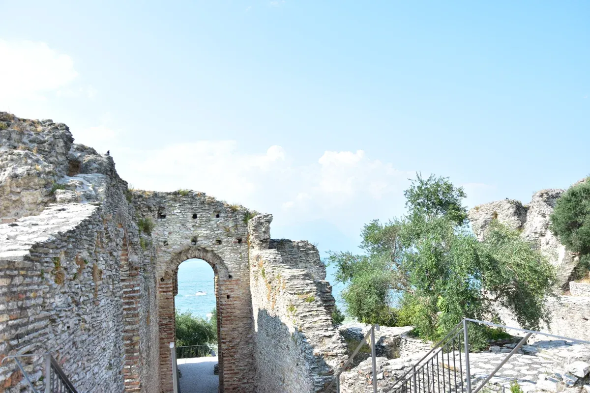 An arch of the Roman villa framing the lake beside olive trees at the Grotte di Catullo, Sirmione, Lake Garda, Italy
