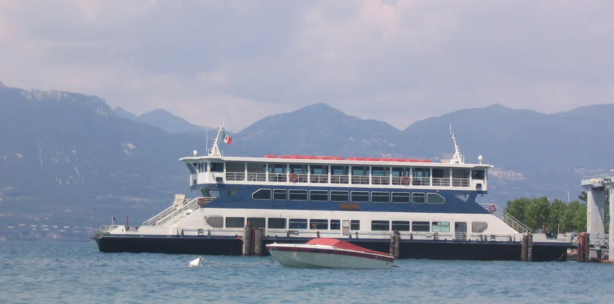 A large Navigazione Laghi ferry at a landing stage on Lake Garda, Italy, with mountains behind