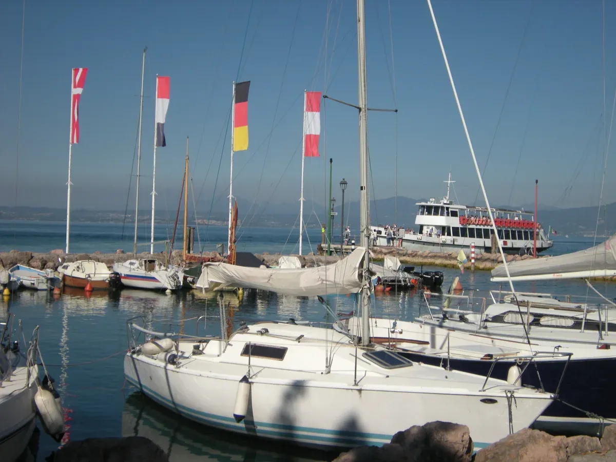 Cisano harbour near Bardolino with a passenger ferry behind the sailing boats on Lake Garda, Italy