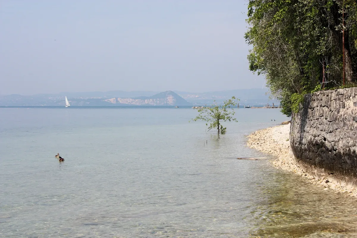 The pebble shore and clear shallow water near Punta San Vigilio, Lake Garda, Italy