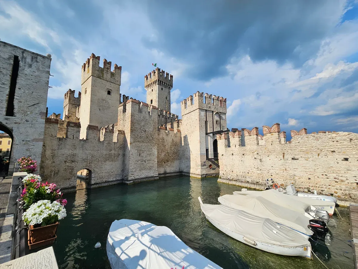The Scaligero Castle of Sirmione rising from its moat with moored boats, Lake Garda, Italy